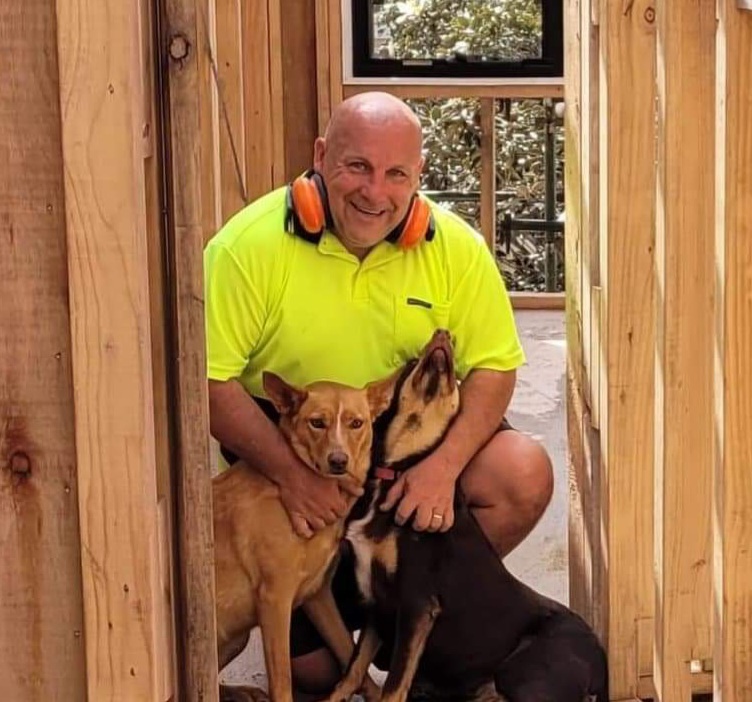 Home Builder Sam Bernardo from Home Building Assist on site with his two dogs, surrounded by house frame and window frame at back